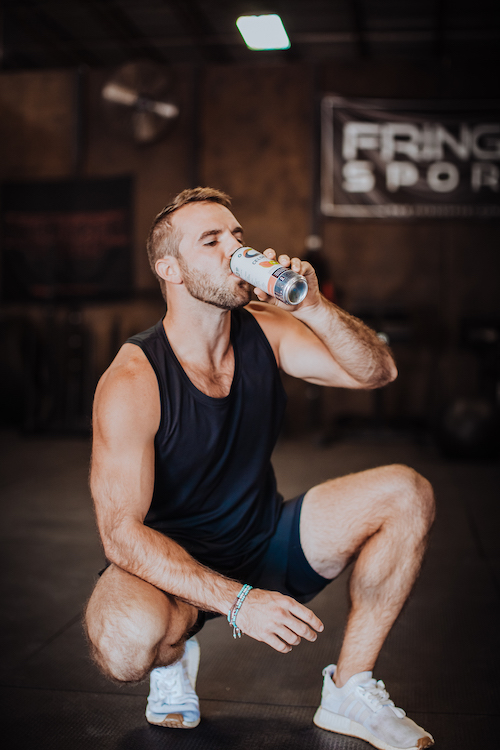 image of a man squatting drinking a celsius